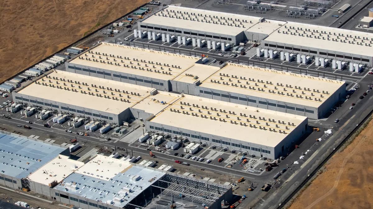 Aerial view of three large AWS data centre buildings with a fourth under construction, surrounded by dry land in Oregon.