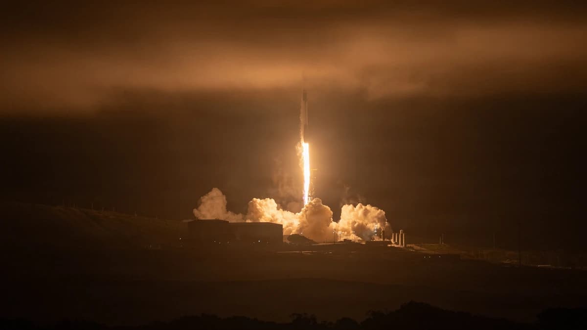 A SpaceX Falcon 9 rocket lifts off at night from a launch pad, its exhaust glowing orange against low cloud