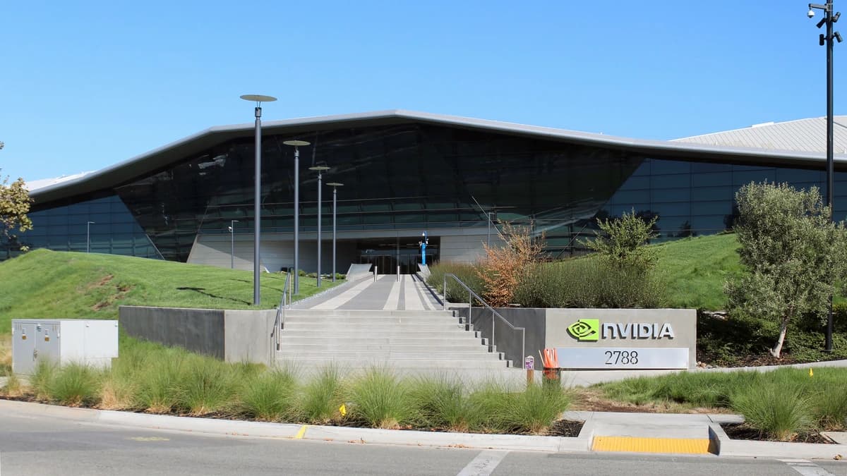 A glass-fronted NVIDIA building with a wide sloping roof, stone steps and a grey sign reading NVIDIA 2788 under a clear blue sky