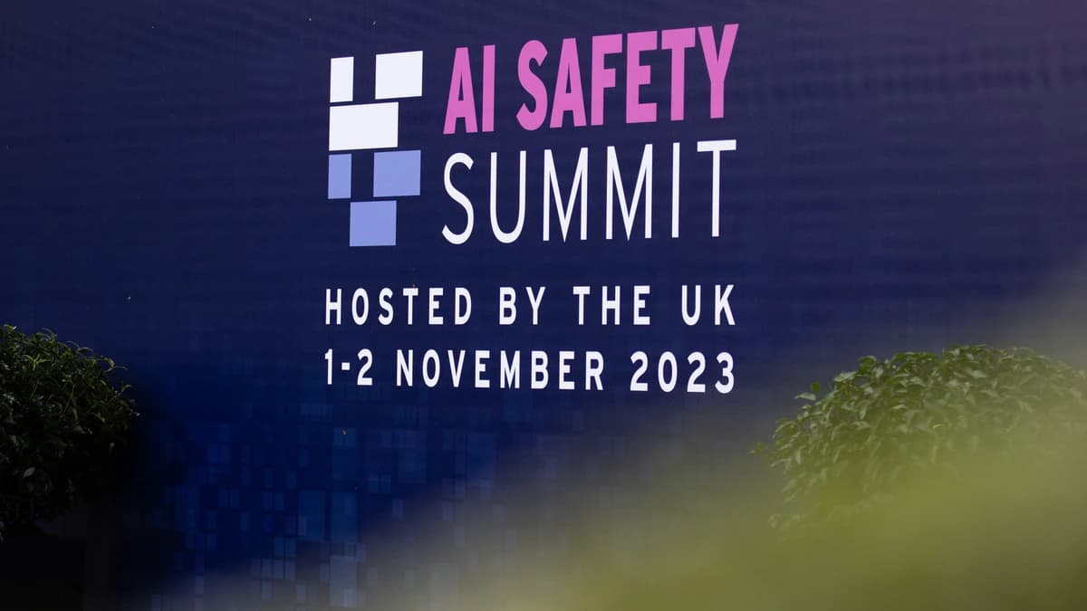 A dark blue event sign reading AI Safety Summit, hosted by the UK, 1 to 2 November 2023, framed by blurred leaves