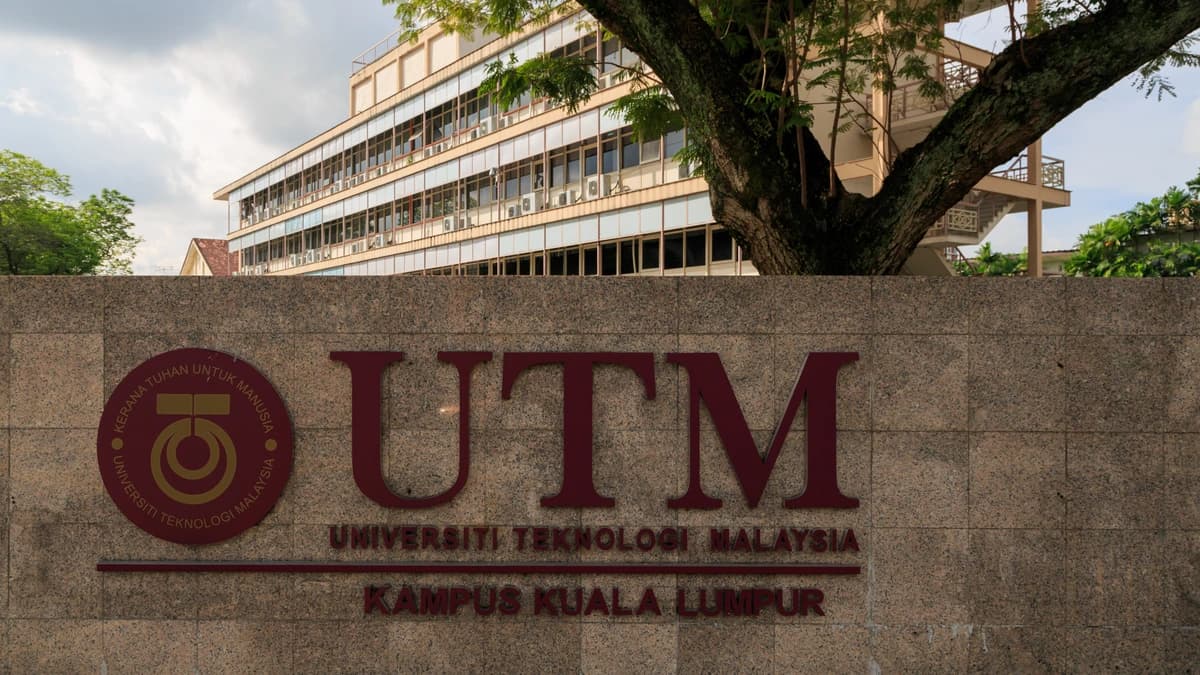 A maroon UTM sign on a stone wall reading Universiti Teknologi Malaysia, Kampus Kuala Lumpur, with a campus building behind it