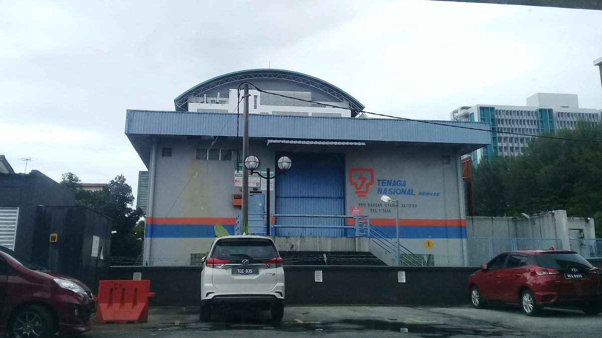 A grey Tenaga Nasional Berhad substation building with a blue roof, red and blue stripes and a sign reading PPU Bandar Utama 33/11kV, with parked cars in front