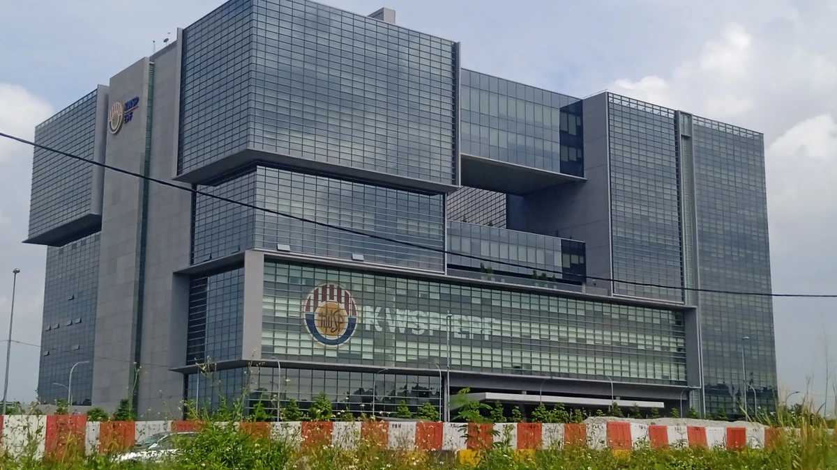 Menara KWSP in Kwasa Damansara, a stacked glass and grey office block with the EPF emblem on its lower facade, rising behind roadside grass and construction hoarding