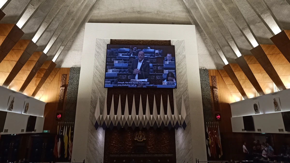 Angled concrete roof ribs above the Dewan Rakyat chamber, with a large screen showing a member speaking below