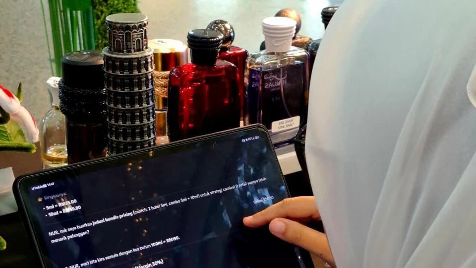 Entrepreneur Nur Batrishya Balkis Abdullah uses Copilot beside perfume products in an AIForMYFuture follow-up photograph