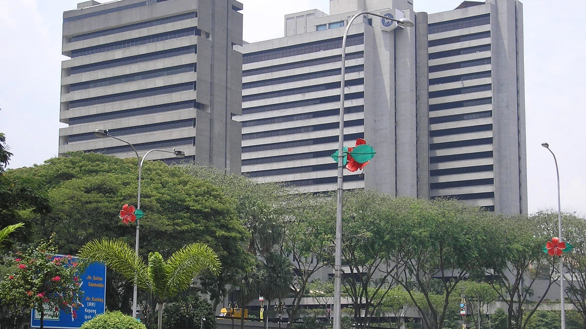 Two grey concrete office blocks of Bank Negara Malaysia's headquarters stand behind green trees and street lamps in Kuala Lumpur