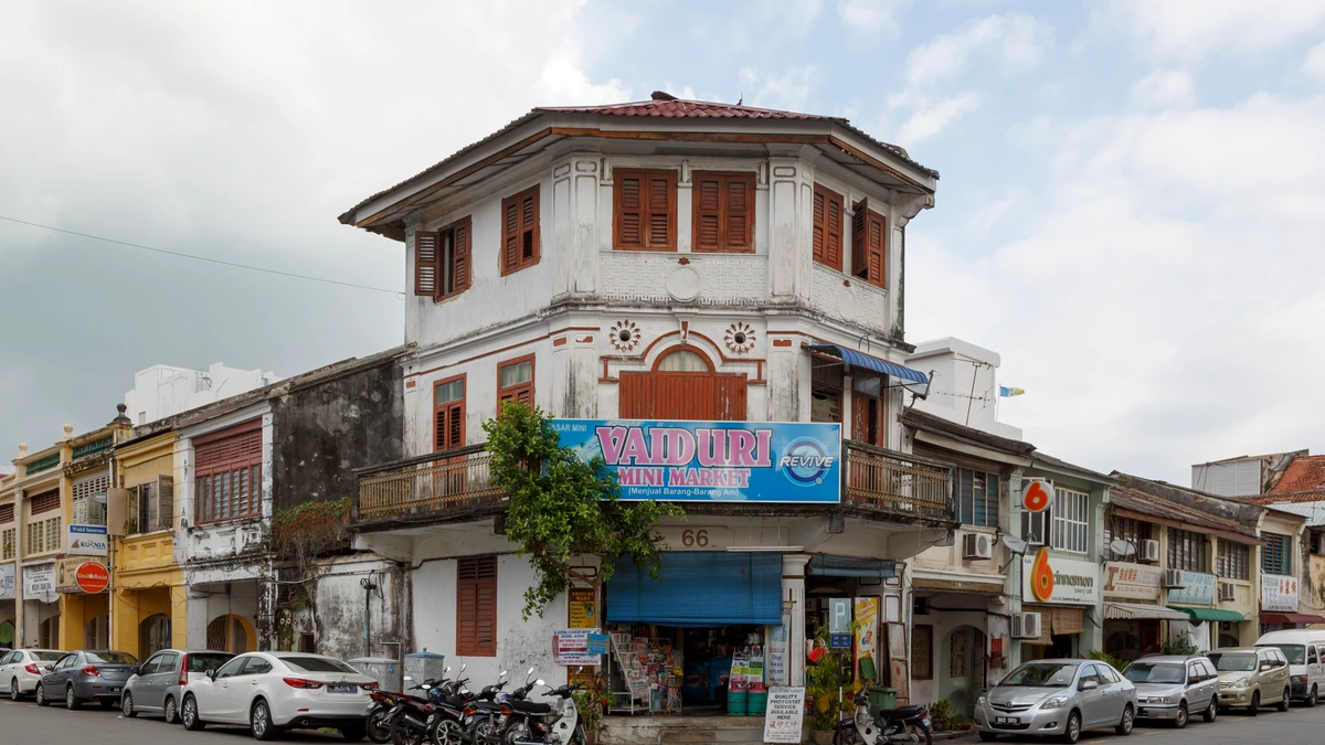 A corner shophouse in George Town, Penang, painted white with timber shutters, a blue mini market signboard across its front and motorcycles parked outside