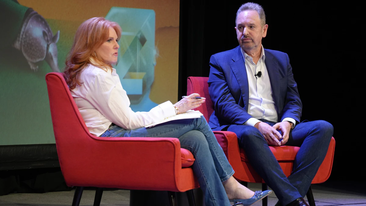 Arm chief executive Rene Haas in a blue suit seated in a red armchair on stage beside interviewer Liz Claman, who holds notes and a pen