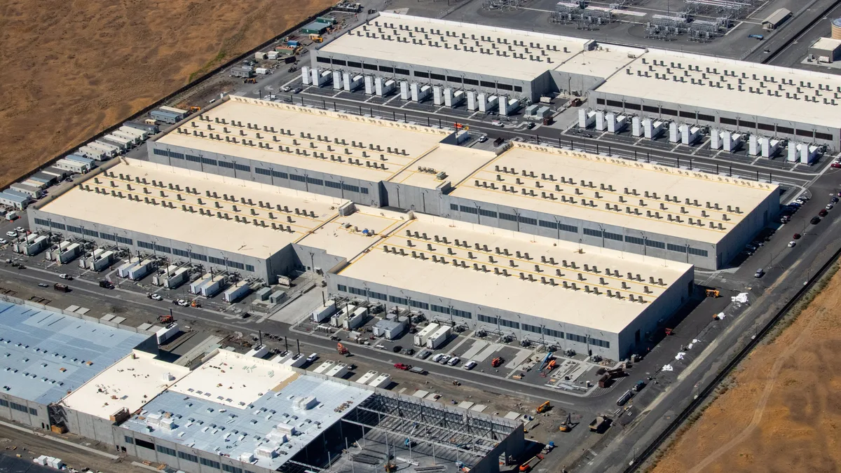 Aerial view of three large AWS data centre buildings with a fourth under construction, surrounded by dry land in Oregon.