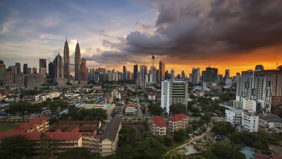 Kuala Lumpur skyline at dusk with the Petronas Twin Towers and KL Tower under a storm-lit orange sky above low-rise housing
