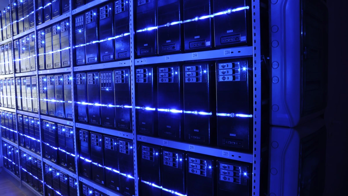 Rows of rack-mounted servers filling a data centre aisle, their front panels lit by blue status lights that stretch away towards the far wall