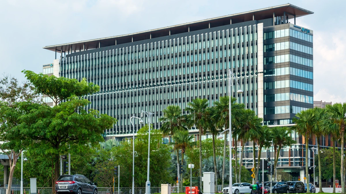 The long louvred glass facade of Menara PjH in Putrajaya seen from across an open forecourt, with palms and young trees along the roadside and parked cars in the foreground