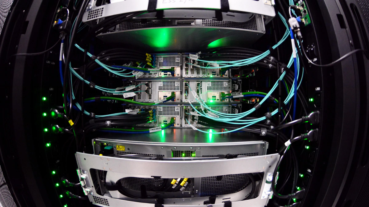 A close wide-angle view into the open rear of a computing rack, showing stacked server sleds, bundles of turquoise and black cabling and rows of green status lights