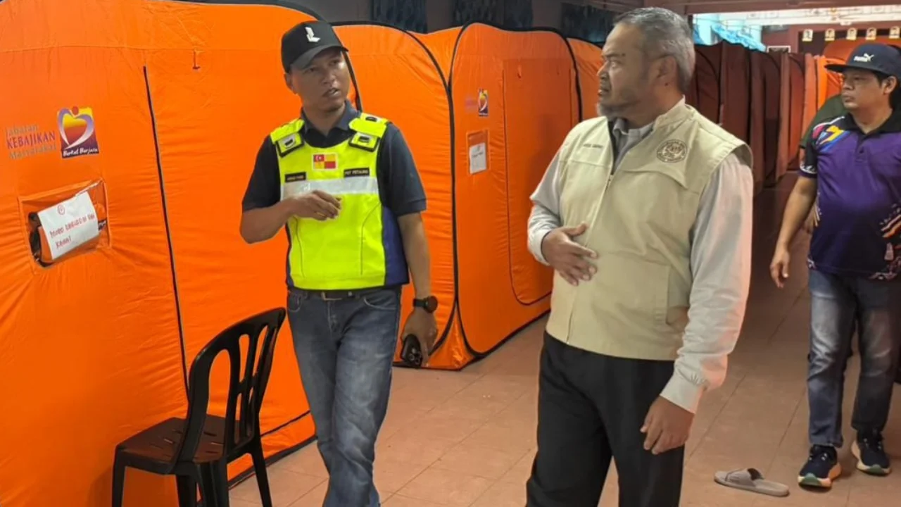 NADMA field officer and local team walk between orange emergency tents at a Selangor evacuation centre