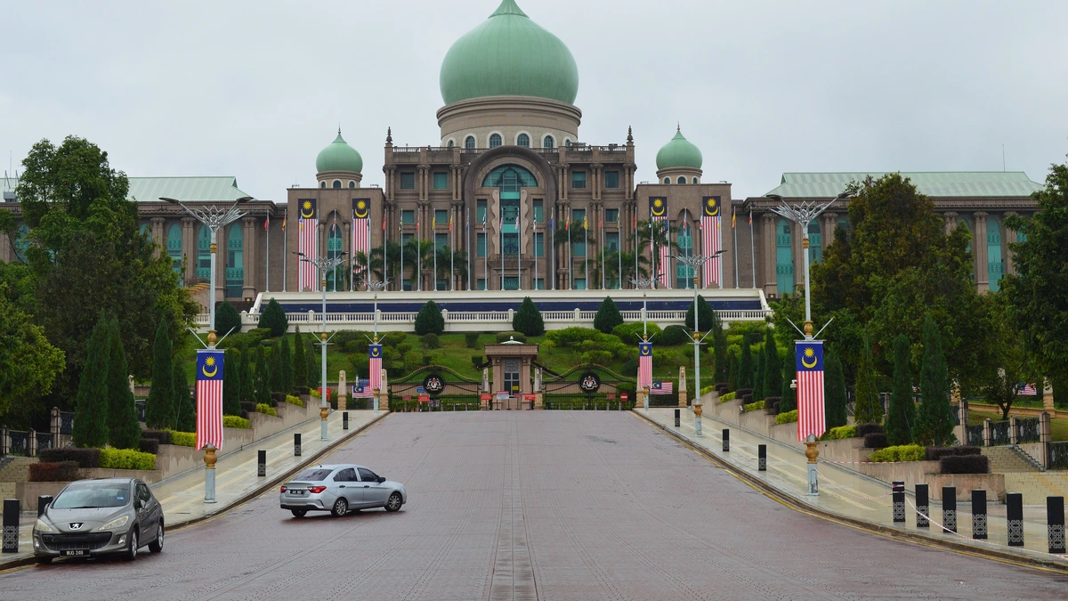 Green-domed Perdana Putra building in Putrajaya at the end of a wide road, with Malaysian flags lining the approach under an overcast sky