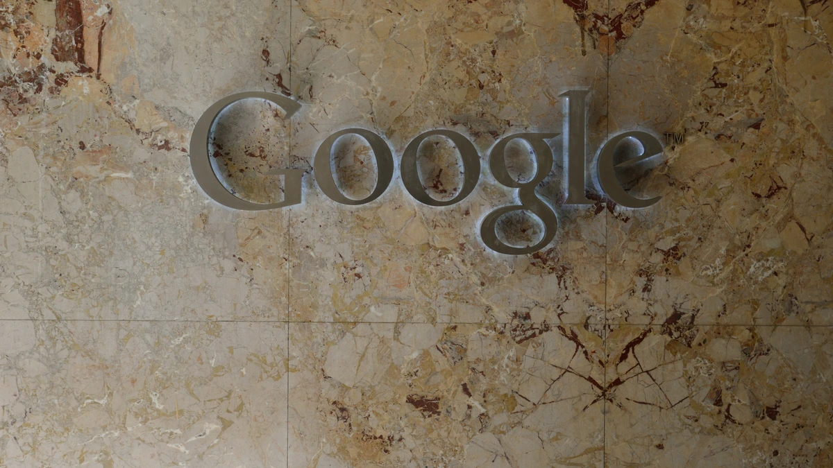 A brushed metal Google wordmark mounted on a polished beige marble wall inside an office lobby