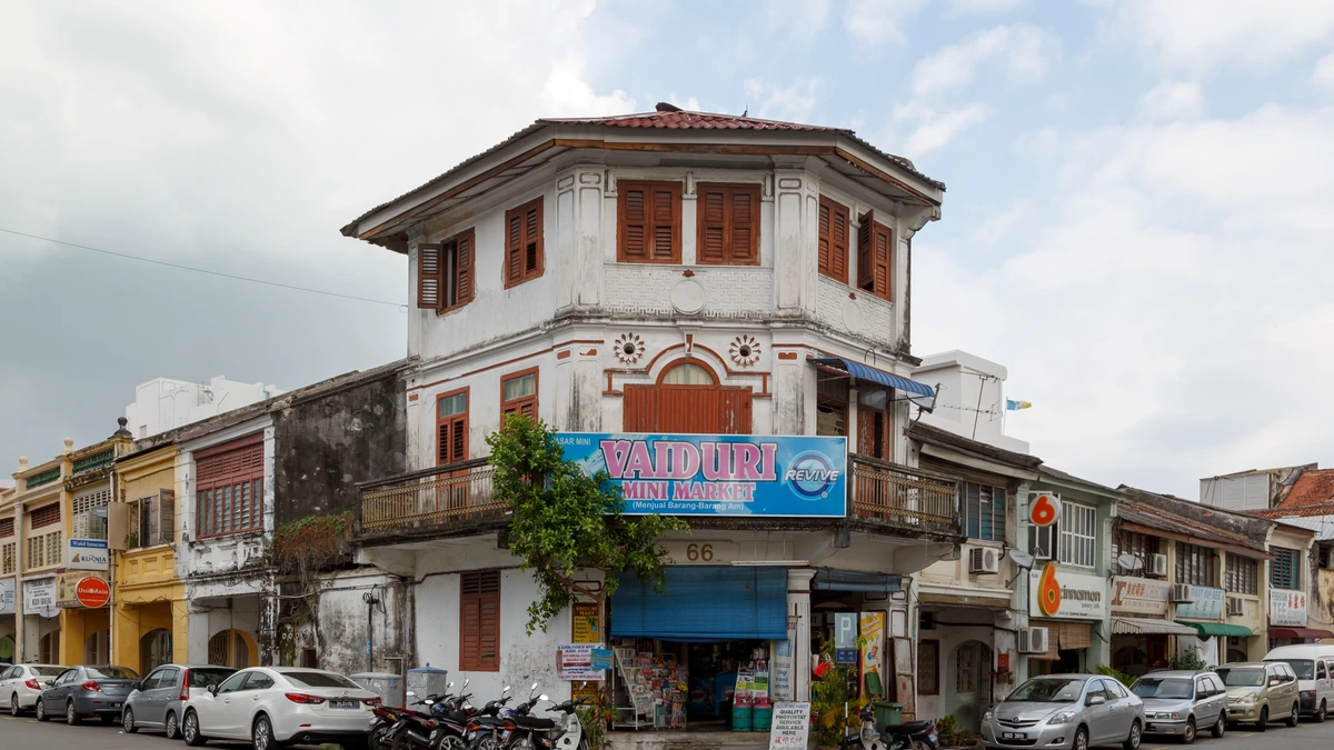 A corner shophouse in George Town, Penang, painted white with timber shutters, a blue mini market signboard across its front and motorcycles parked outside