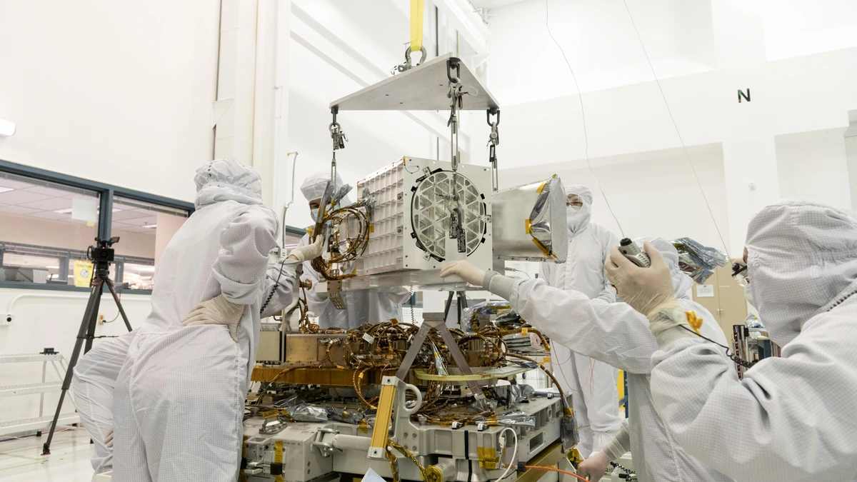 Engineers in cleanroom suits guiding EMIT's optical subsystem, a white cube holding its telescope and imaging spectrometer, down onto the instrument's electronics baseplate
