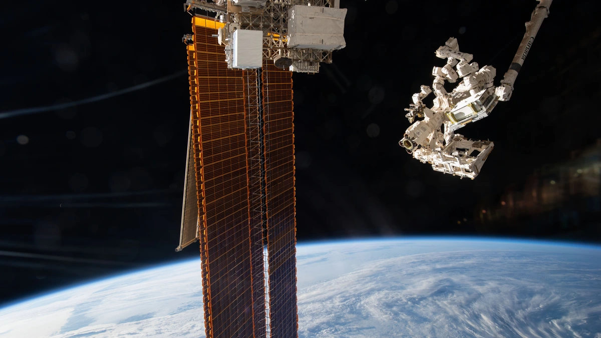 The International Space Station's Canadarm2 robotic arm holding the EMIT instrument above a cloud-covered Earth after removing it from a SpaceX Dragon cargo craft
