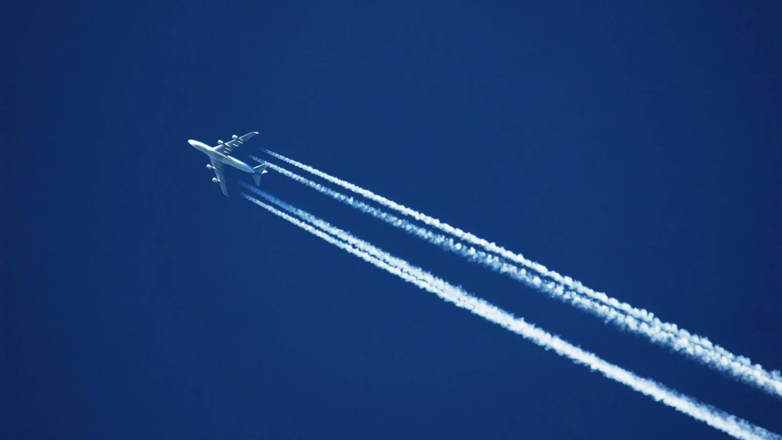 Commercial aircraft crosses a clear blue sky while producing four visible contrails