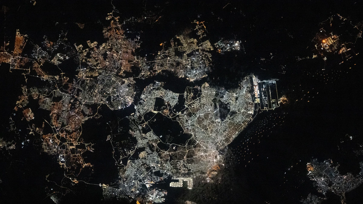 Night view from orbit of Singapore and Johor Bahru, with glowing street grids on either side of a dark strait
