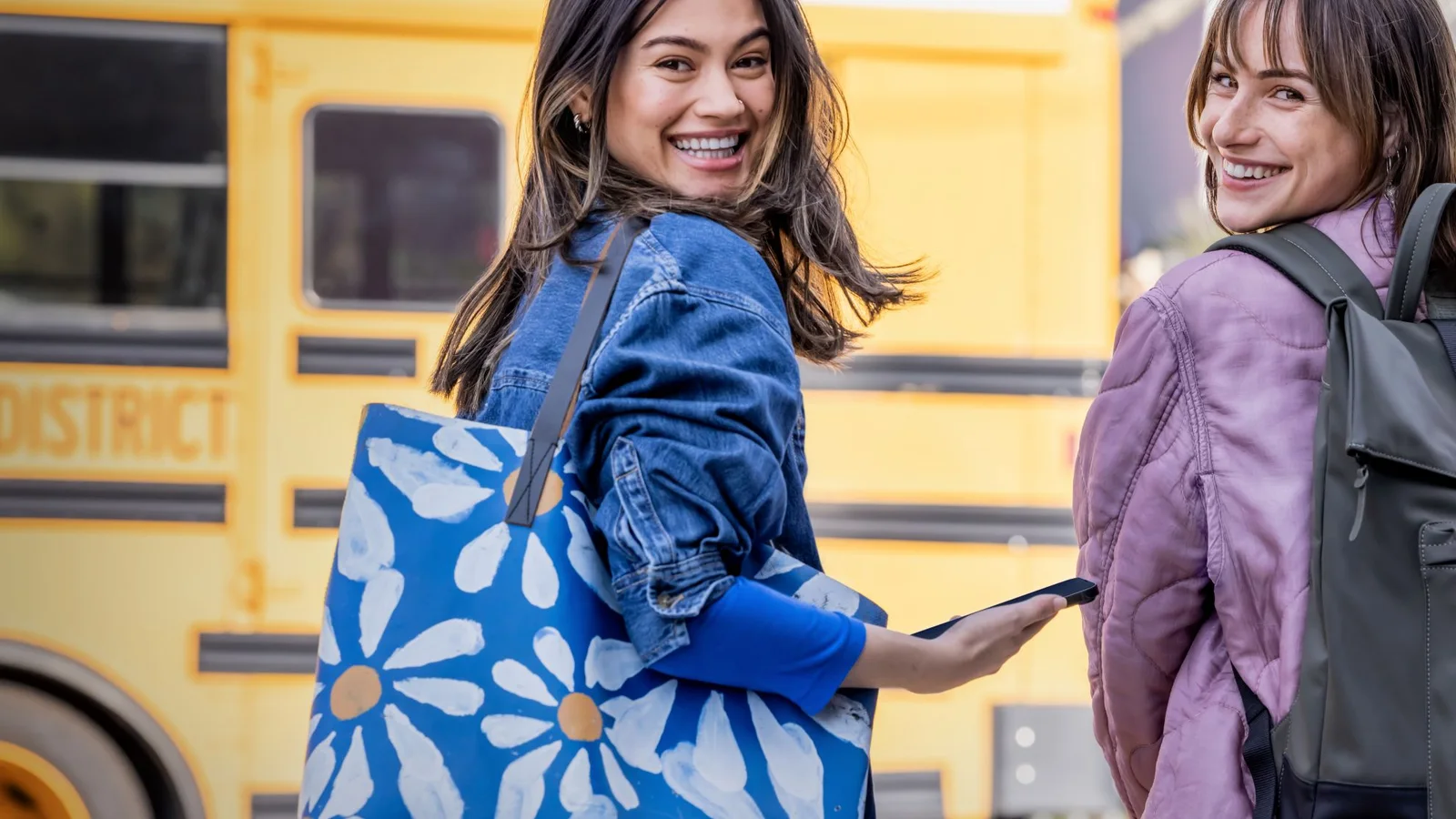 Two students carrying bags beside a yellow school bus in an official Microsoft Education photograph