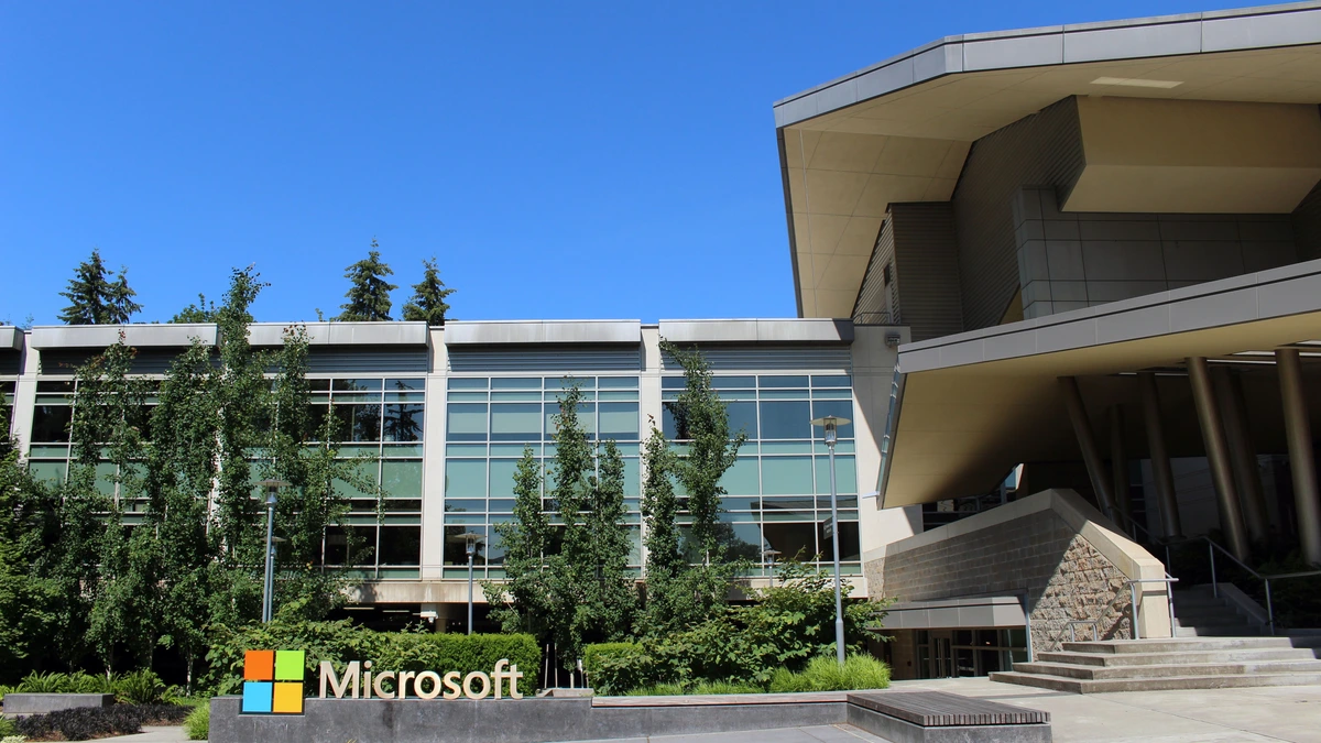 A glass and concrete Microsoft office building with the four-colour Microsoft logo on a low stone sign among trees