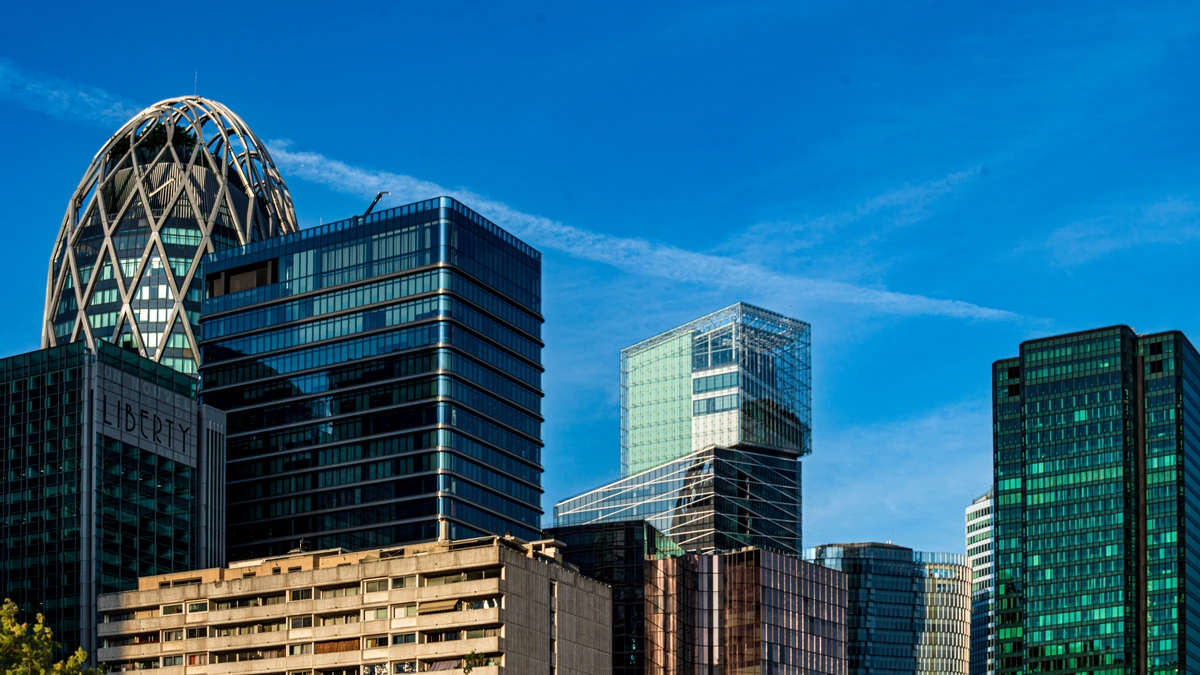 Glass office towers at La Défense in Paris, including a tower with a lattice dome, under a blue sky with a thin white contrail