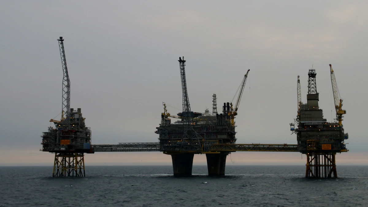 Three offshore platforms linked by long connecting bridges stand on steel and concrete legs in a calm grey sea at dusk, with cranes and a flare tower rising above the decks