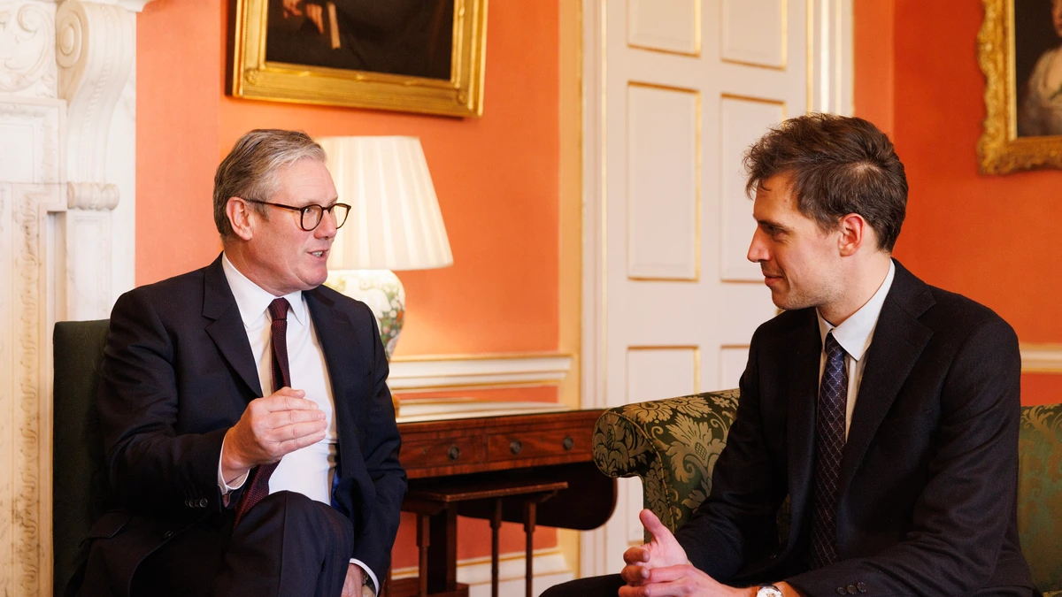 Mistral chief executive Arthur Mensch in a dark suit and tie seated on a sofa, listening to UK Prime Minister Keir Starmer in an orange-walled room hung with portraits