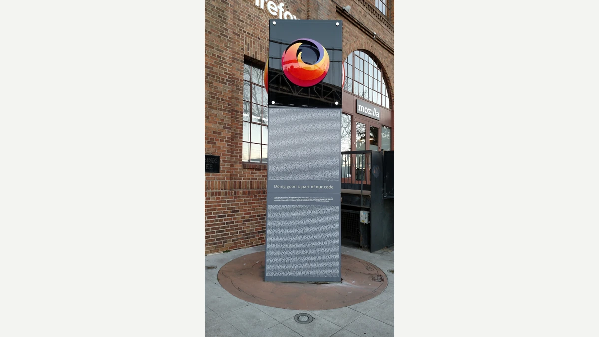 A tall black and grey monument sign with the Firefox logo and the words Doing good is part of our code, standing on a pavement in front of a red-brick building marked mozilla