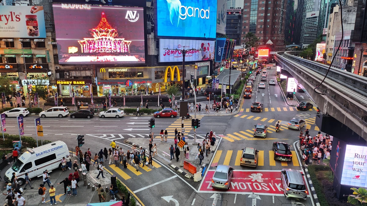 Pedestrians cross the busy Bukit Bintang junction in Kuala Lumpur beside large digital billboards