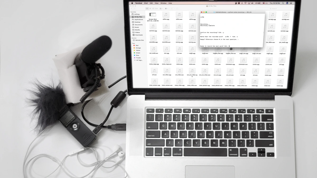 A microphone, a handheld audio recorder and earphones connected to a laptop showing a folder of audio files