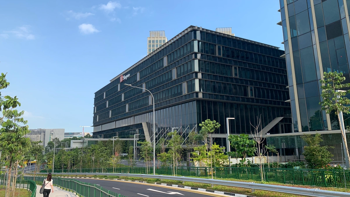 The Shopee Building at 5 Science Park Drive in Singapore, a long dark glass office block with a small Shopee sign near the roofline, seen across a curving road and footpath under a blue sky