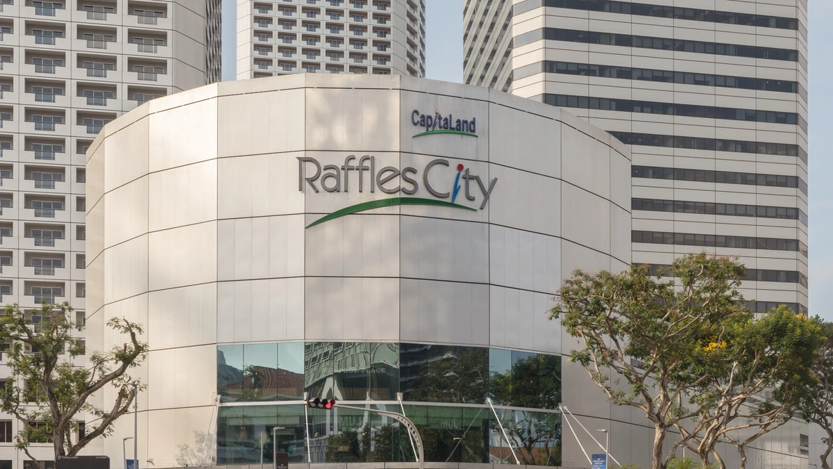 Raffles City in Singapore, a curved white building with Raffles City and CapitaLand signs, standing in front of two tall striped towers and a hotel block under a pale sky