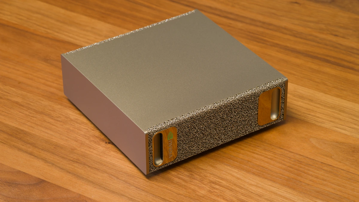 A silver-gold box with a foam-metal front panel and two recessed handles sits at an angle on a wooden table