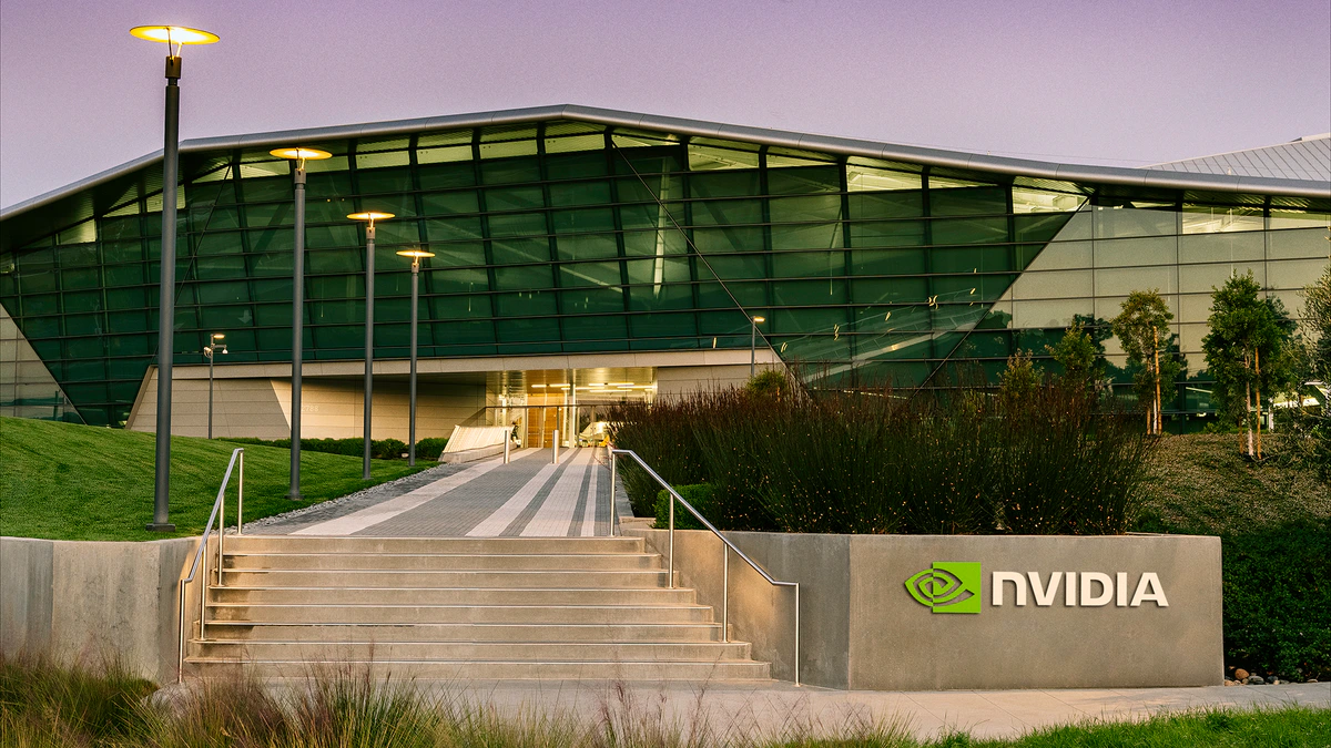 NVIDIA's Endeavor building at dusk, a low glass structure with an angular roof, seen from a stepped walkway beside a logo sign