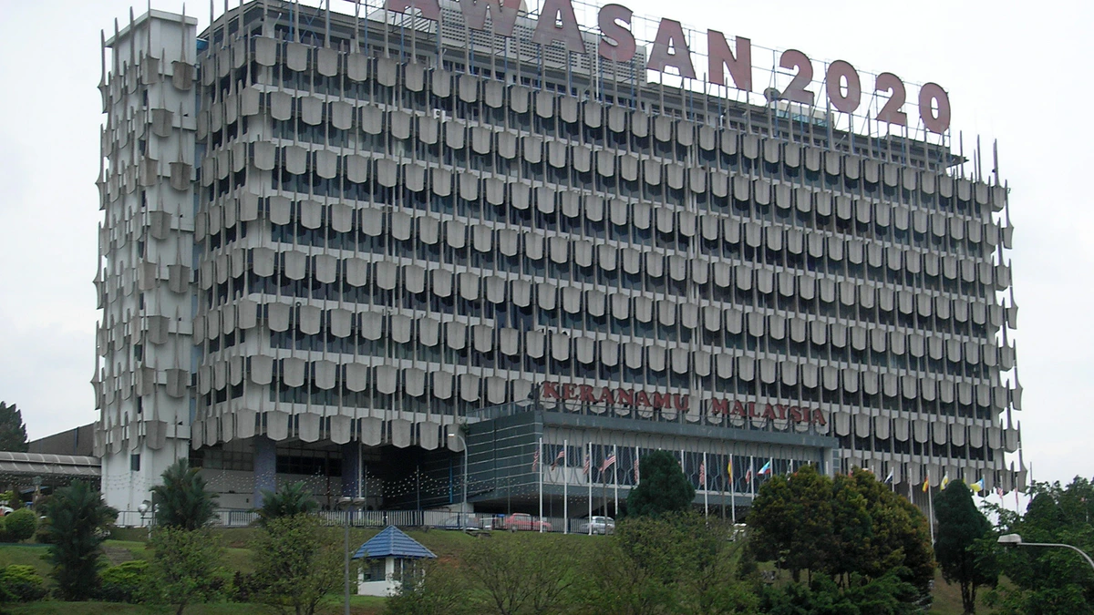 The long curved concrete facade of Angkasapuri in Kuala Lumpur, its rows of shaped window hoods stacked across ten floors, with WAWASAN 2020 lettering on the roof and flags along the entrance