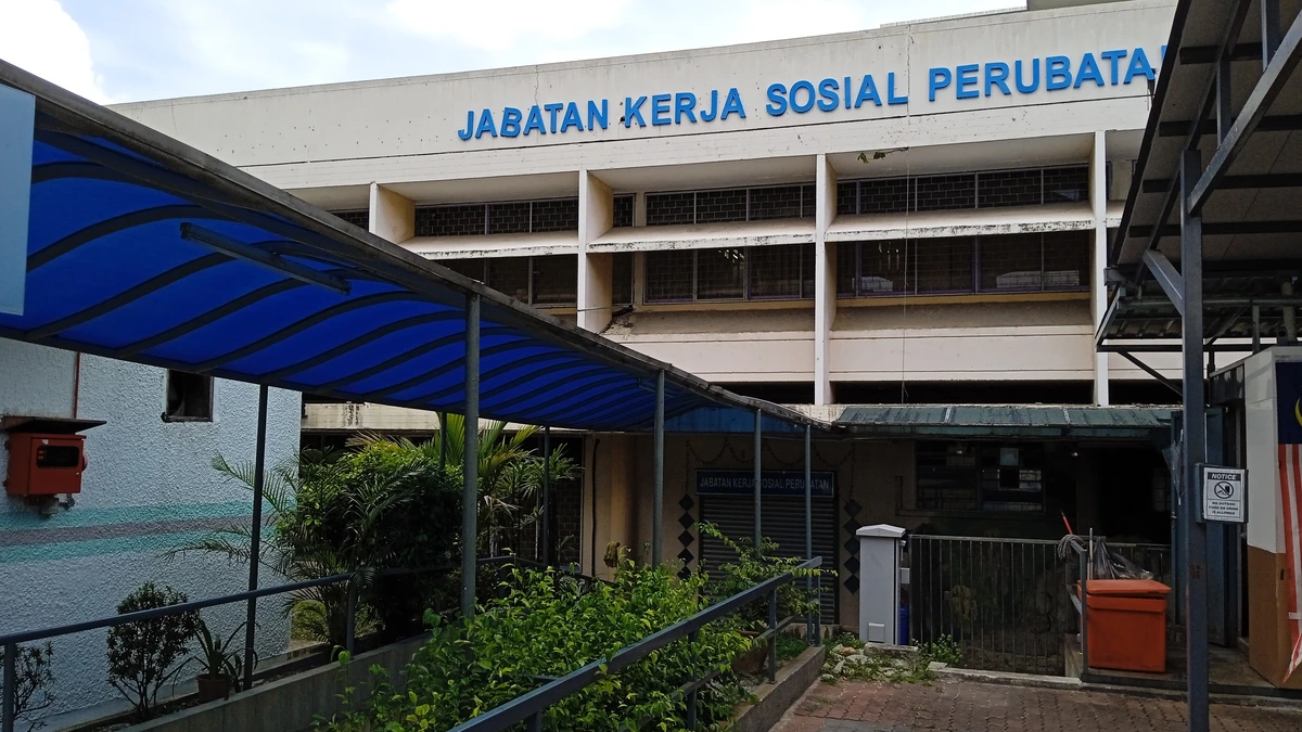 The Medical Social Work Department building at Hospital Kuala Lumpur, its name in blue capital letters on a white facade, reached by a covered walkway lined with potted plants