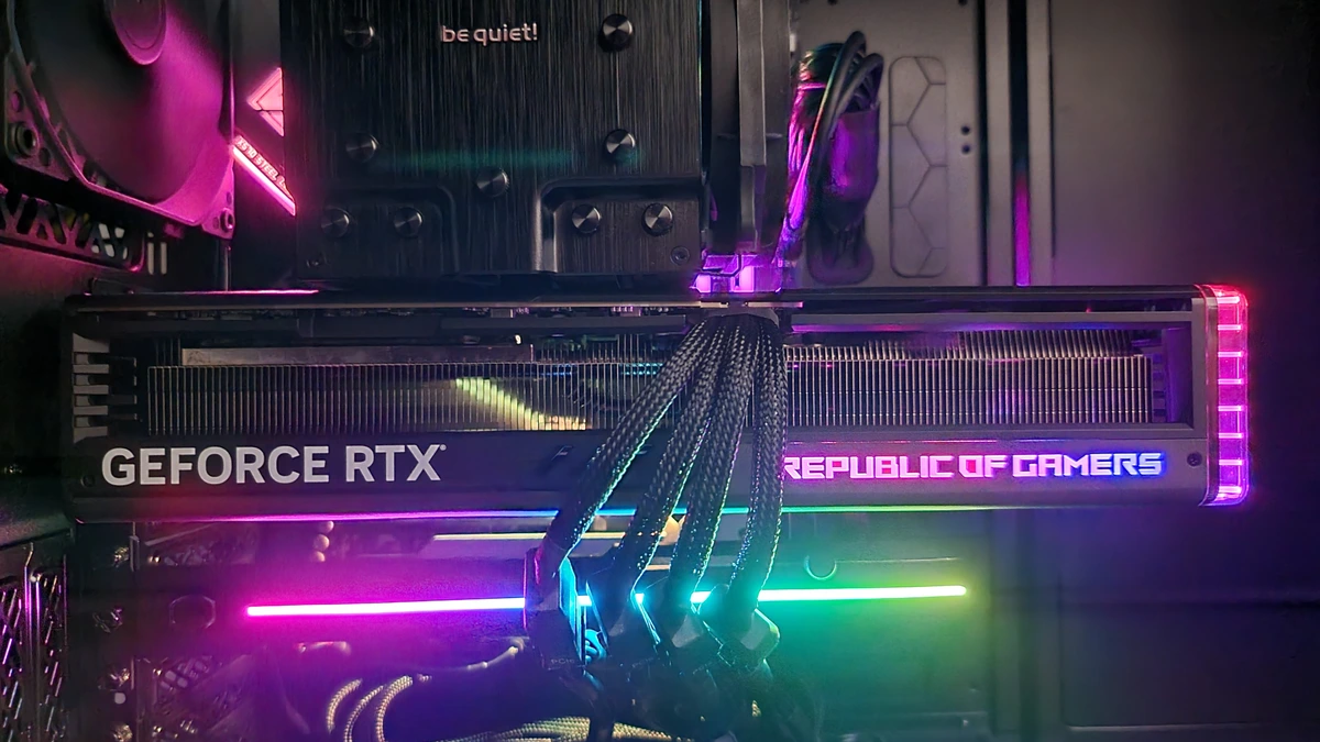 An Asus ROG Strix GeForce RTX graphics card lit in pink and green light, installed horizontally inside a desktop PC with braided power cables plugged into its top edge