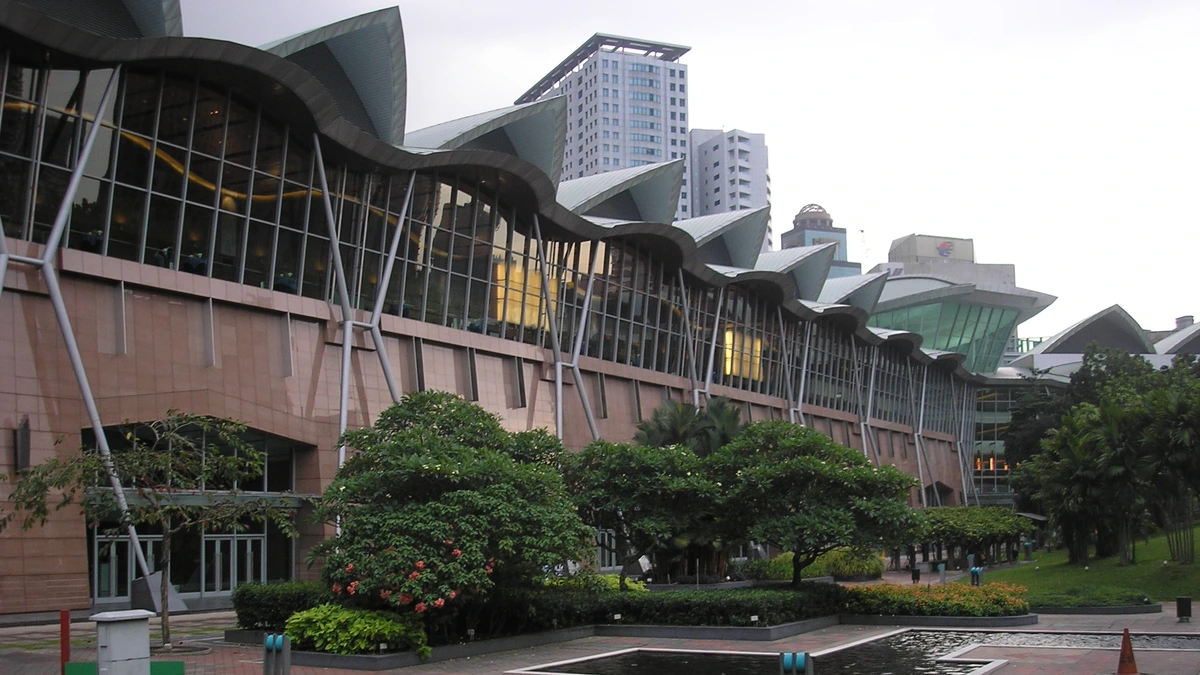 Wave-shaped roofline and glass wall of the Kuala Lumpur Convention Centre beside a garden with a small pond