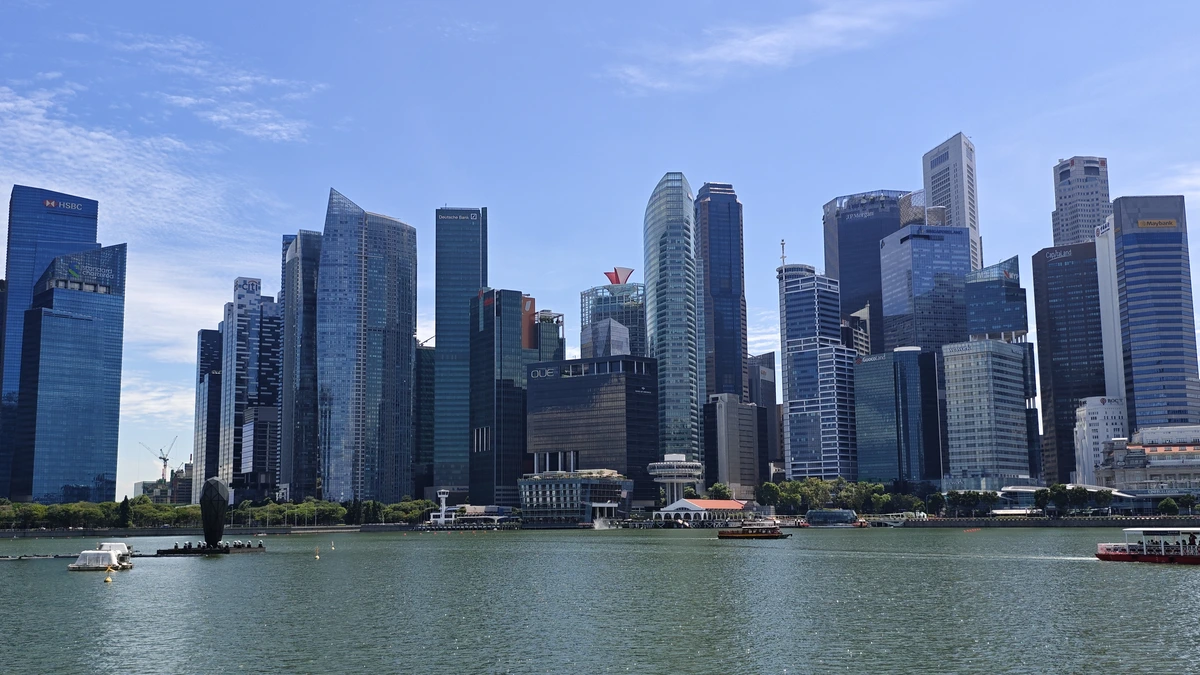 The Singapore central business district seen across Marina Bay on a clear day, with dense glass and stone office towers behind the waterfront and small boats crossing the water in front