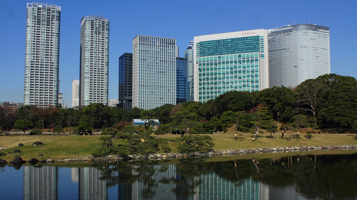 Glass and concrete office towers in Tokyo’s Shiodome district reflected in a pond under a clear blue sky