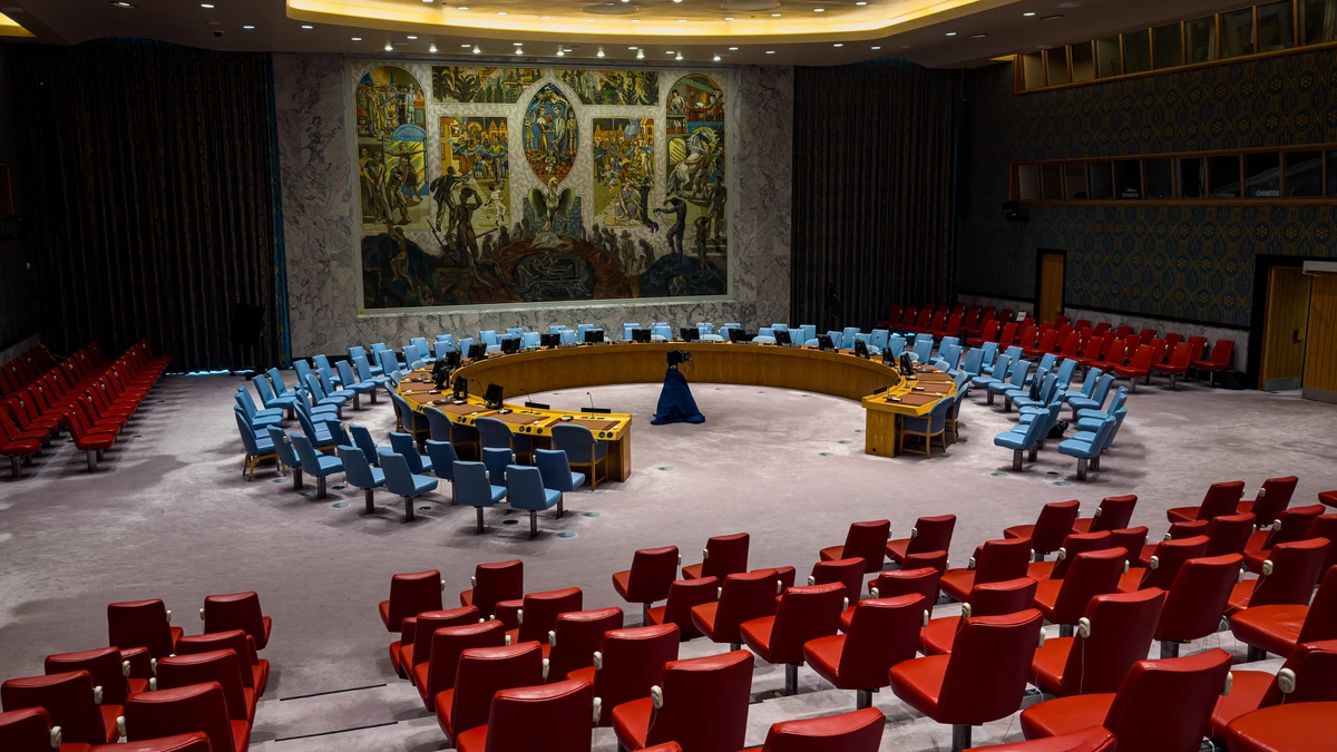 The empty UN Security Council chamber in New York, with the horseshoe-shaped table and blue delegate chairs in front of Per Krohg's large mural, and rows of red gallery seats in the foreground