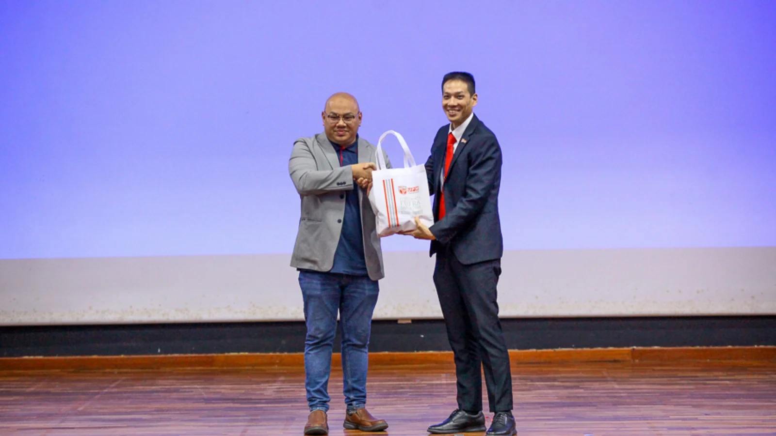 Two representatives exchange a Universiti Putra Malaysia token during a workplace-safety technology event