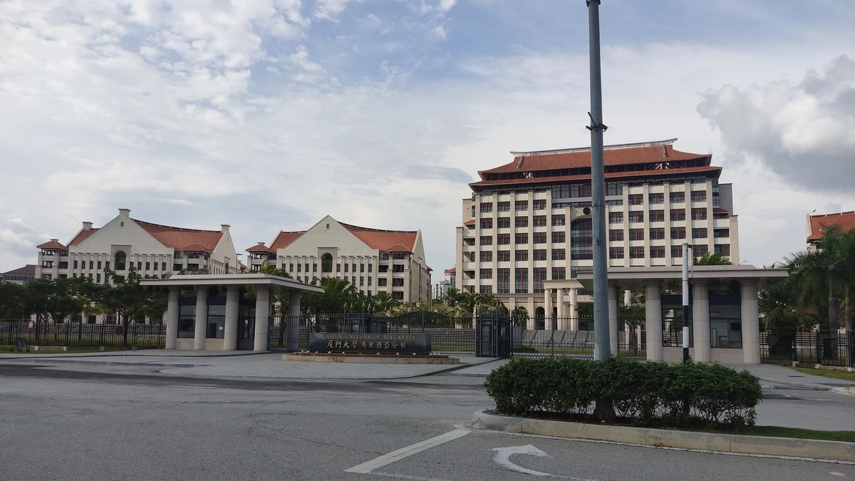 Entrance gate and cream campus buildings with red tiled roofs at Xiamen University Malaysia under a cloudy sky