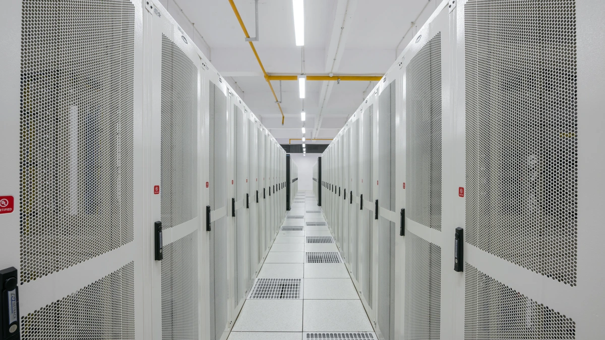 A long white aisle between tall perforated-door server racks under bright ceiling lights