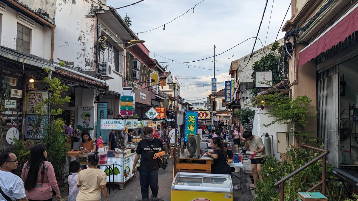 Visitors and stallholders fill Jalan Hang Kasturi in Melaka's old town during the Jonker Street night market, with food carts, an ice-cream freezer, shophouses and hanging Chinese signboards under an evening sky