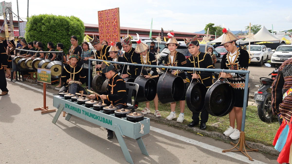 Young Kadazan musicians from Papar in black costumes with gold trim and conical hats play a row of hanging gongs and a kulintangan set at a roadside procession in Sabah